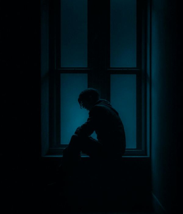 Person meditating peacefully near a large window with soft light.